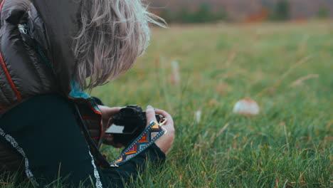 Close-up-shot-of-a-woman-with-grey-hair-from-behind-lying-on-the-grass-and-taking-photos-of-a-mushroom-in-nature-during-a-cold-windy-day-in-autumn