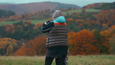 Medium-shot-of-a-female-Photographer-taking-pictures-of-beautiful-autumn-natures-with-bright-orange-colors-with-her-camera-and-walking-through-the-field-during-a-windy-day-in-slow-motion