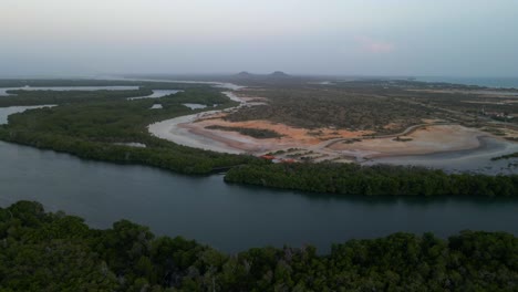 Drone-flies-above-a-mangrove-forest-crossing-an-extended-estuarine-river-revealing-a-shoreline,-beautiful-horizon-with-Tetas-de-Maria-Guevara-mountains,-Porlamar,-Margarita-Island,-Venezuela