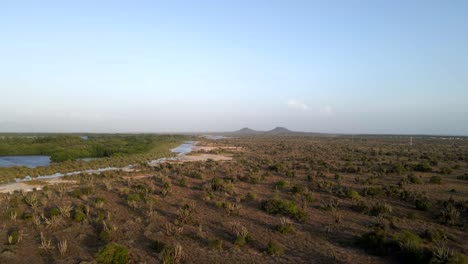 Drohne-Bewegt-Sich-über-Einer-Riesigen-Landfläche-Und-Zeigt-Auf-Der-Linken-Seite-Ein-Großes-Gewässer,-Zwei-Berge-Am-Horizont,-Wie-Dieses-Wunderschöne-Grasland-In-Porlamar,-Insel-Margarita,-Venezuela