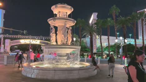 People-walking,-a-father-plays-with-a-child-and-water-is-flowing-in-slow-motion-at-the-fountain-on-the-Strip-in-Las-Vegas,-night