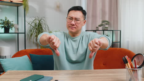 Upset-Chinese-man-showing-thumbs-down,-dislike-bad-work,-disapproval-dissatisfied-feedback-at-home