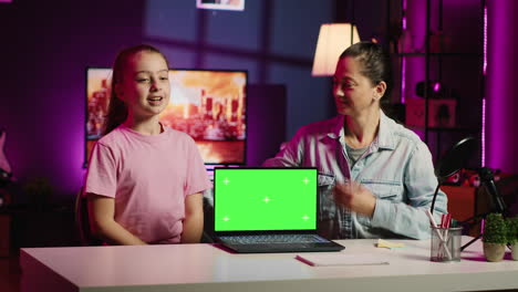 Daughter-and-mother-in-home-studio-film-video-together-next-to-green-screen-laptop