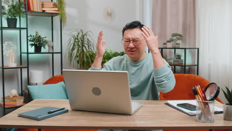 Angry-Asian-man-use-laptop-surprised-by-bad-news,-fortune-loss,-game-fail,-lottery-results-at-home