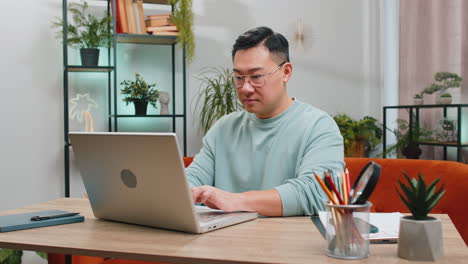 Hombre-Asiático-Concentrado-Y-Confiado-Que-Trabaja-Remotamente-En-Un-Proyecto-En-Una-Computadora-Portátil-En-La-Habitación-De-Casa