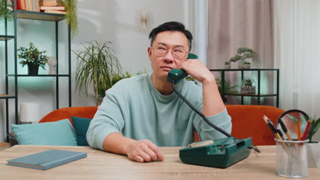 Cansado-Y-Aburrido-Hombre-Asiático-Hablando-Por-Teléfono-Con-Cable-Agotado-De-Hablar,-Haciendo-Muecas,-Engañando