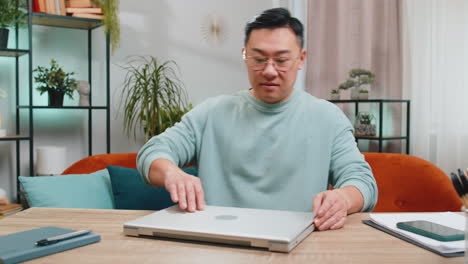 Asian-mature-man-freelancer-starts-working-on-laptop,-sends-messages,-makes-online-purchases-at-home