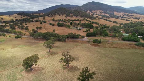 Over-trees-in-paddocks-towards-a-road-with-a-farmhouse-in-the-background-near-Eildon,-Victoria,-Australia