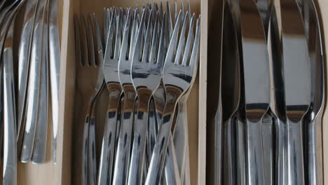 Top-shot-of-an-open-kitchen-drawer,-putting-two-forks-into-the-drawer