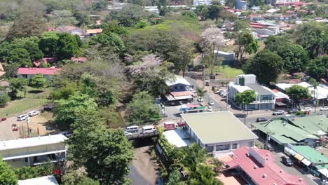 Costa-Rica-beach-drone-flying-over-Jaco,-a-typical-central-american-town-with-small-houses,-a-river-and-sorrounded-by-a-forest-with-the-green-mountain-at-the-horizon-on-a-sunny-day