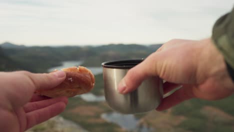 A-Person-Holding-A-Stainless-Steel-Vacuum-Flask-Coffee-Cup-And-Bread-Over-Mountains