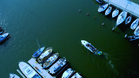 Aerial-perspective-of-a-small-motorboat-moving-through-the-water-near-a-dock-with-various-moored-boats-on-one-side