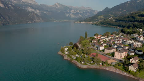 Forward-moving-aerial-shot-with-small-village-and-camping-ground-on-the-foreground,-mountain-lake-in-background