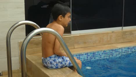 A-small-young-boy-sitting-wet-outside-a-swimming-pool-shivering-from-the-cold-one-feels-after-getting-out-of-the-water