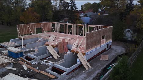 Drone-shot-of-housing-construction-site-in-the-evening-with-wood-framing-and-concrete-basement-in-progress