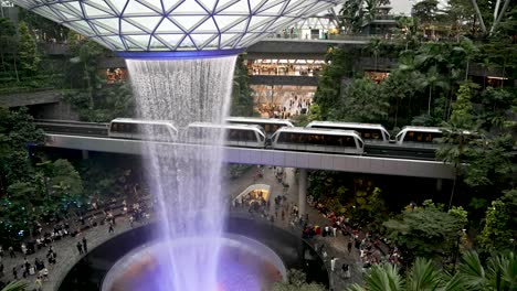 High-Angle-View-Overlooking-The-Rain-Vortex-Indoor-Waterfall-At-Jewel-Changi-Airport-Singapore-With-Skytrain's-Going-Past