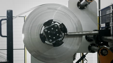 Side-shot-of-a-roll-of-sheet-metal-being-pulled-off-in-an-automated-car-parts-factory