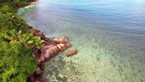 slow-moving-drone-shot-of-Indian-ocean,-granite-rocks,-trees-and-turquoise-water-on-the-baie-lazare-shore,-Mahe-Seychelles-30-fps