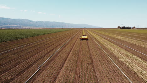 Slow-Motion-wide-drone-of-artichoke-farm-field-and-weeding-machine-moving-forwards