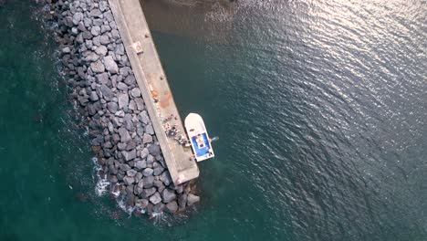 Rotierende-Draufsicht-Auf-Ein-Festgemachtes-Fischerboot-Am-Docksteg-Mit-Touristen-Im-Sommer,-Azoren,-Porto-Formoso