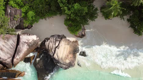 Bird-eye-drone-shot-of-white-sandy-beach,-large-granite-stone,-trees-and-waves-crashing-on-the-shore,-Mahe-Seychelles-60-fps-3