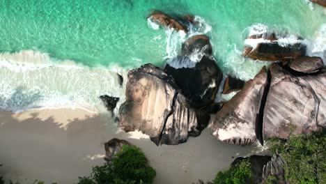 Bird-eye-drone-shot-of-white-sandy-beach,-large-granite-stone,-trees-and-waves-crashing-on-the-shore,-Mahe-Seychelles-60-fps-2