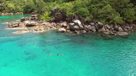 Drone-of-Anse-major-beach,-2-woman-snorkelling,-granite-stones,-turquoise-water,-Mahe-Seychelles-60-fps