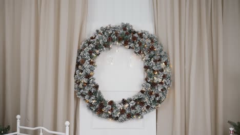 Large-snow-dusted-pinecone-wreath-with-twinkly-lights-on-Christmas-set