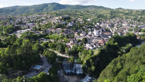 Jajce-city-establishing-aerial-view-of-stunning-Pliva-waterfall-cascading-below-Bosnia-and-Herzegovina-lush-mountain-valley-scenery