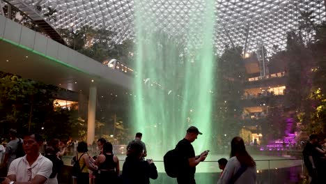 Rain-Vortex-Waterfall-Located-At-Jewel-Changi-Airport-With-Green-Light-Glow-And-Skytrain-Going-Past-Overhead
