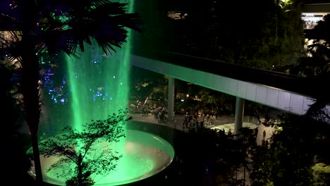 High-Angle-View-Overlooking-Green-Illuminated-Indoor-Waterfall-At-Jewel-Changi-Airport-Singapore-In-The-Evening