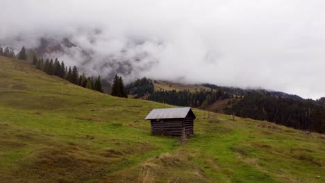 Small-wooden-hut-in-Austria-mountains,-aerial-pull-back-reveal-landscape,-Hochkonig