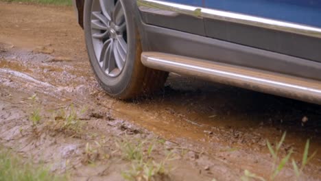 Car-passing-through-a-dirt-road,-navigating-through-a-mud-puddle