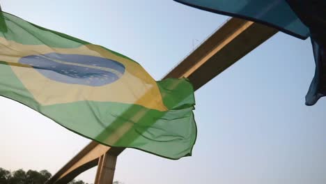 Die-Nationalflaggen-Brasiliens-Und-Paraguays-Wehen-Im-Wind-Und-Tanzen-Harmonisch-Vor-Dem-Hintergrund-Der-Brücke,-Die-Brasilien-Und-Argentinien-Verbindet