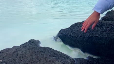Woman-touching-the-turquoise-thermal-water-among-volcanic-rocks