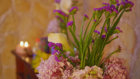 A-dynamic-pan-shot-captures-a-soothing,-relaxing-environment-with-a-colorful-bouquet-of-blooming-flowers-sets-against-a-background-of-natural-stone-and-candles-with-a-pleasing-shallow-depth-of-field