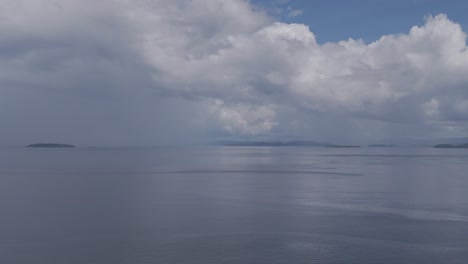 Large-moody-grey-storm-clouds-over-a-calm-seascape-with-small-islands-in-the-far-distance