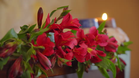 Flores-Rojas-Que-Florecen-Con-Una-Suave-Y-Relajante-Luz-De-Velas-Contra-La-Pared-De-Piedra