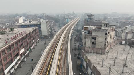Parallaxenaufnahme-Aus-Der-Luft-Entlang-Einer-Leeren-Orangefarbenen-U-Bahn-Strecke-In-Lahore-Mit-Dunstiger-Luftverschmutzung-Im-Hintergrund