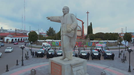 Vertical-pan-of-7-police-pick-ups-and-2-ambulances-with-armed-officers-of-the-Police-Department-lined-up-and-posing-in-front-of-their-cars-and-behind-a-statue-of-President-Benito-Juarez
