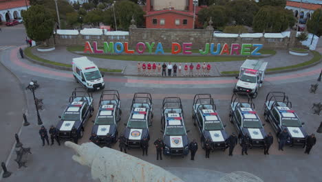 Forward-moving-shot-passing-a-statue-and-ending-on-7-police-pick-ups-and-2-ambulances-with-armed-officers-of-the-Police-Department-lined-up-and-posing-in-front-of-their-cars