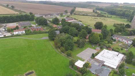 Moving-drone-footage-of-a-very-small-village-in-rural-Yorkshire,-England,-UK-including-a-school,-farm,-church,-houses,-all-surrounded-by-fields-and-countryside