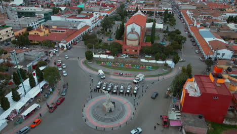 High-altitude-tracking-shot-of-7-police-pick-ups-and-2-ambulances-with-armed-officers-of-the-Police-Department-lined-up-and-posing-in-front-of-their-cars-and-behind-a-statue-of-President-Benito-Juarez