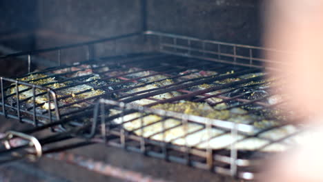 Galjoen-barbecue-on-grid-over-open-fire-with-rising-smoke,-closeup-rack-focus