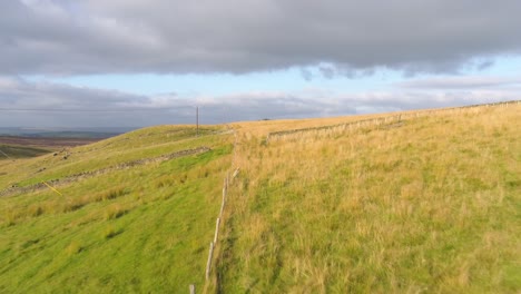 Drone-footage-following-the-path-of-a-farmer's-fence-over-fields-and-moorland-in-West-Yorkshire,-UK,-England-at-golden-hour-in-the-evening