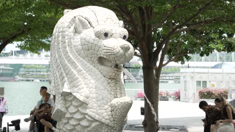 Mini-Merlion-Skulptur-In-Singapur-Mit-Touristen,-Die-Unter-Einem-Baum-Im-Hintergrund-Sitzen