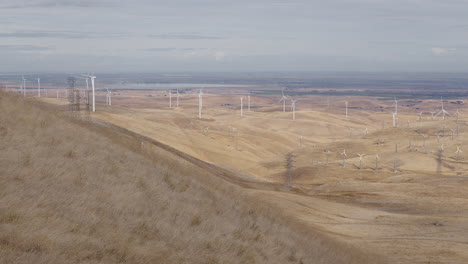 Wide-shot-of-dry-hills-with-windmills-turning-in-the-background-on-a-cloudy-day