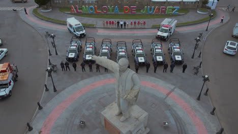 Birdseye-downshot-of-7-police-pick-ups-and-2-ambulances-with-armed-officers-of-the-Police-Department-lined-up-and-posing-in-front-of-their-cars-and-behind-a-statue-of-President-Benito-Juarez