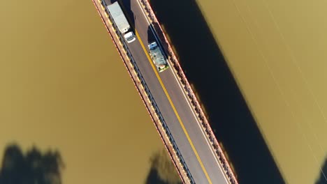 Drone-footage-ascending-and-panning-over-a-bridge-spanning-a-brown-river-with-cars-passing-by