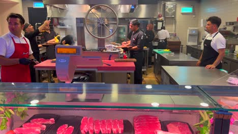 Open-kitchen-and-meat-store-at-a-restaurant-with-fresh-raw-meat-and-many-people-working-and-cooking,-butcher-shop,-4K-shot